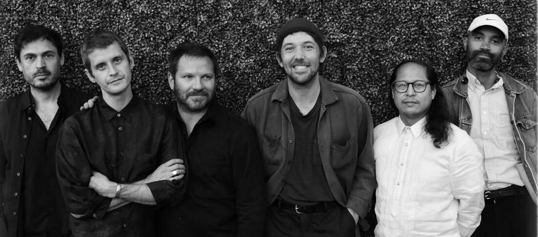 Black and white photo of Fleet Foxes standing in front of a wall of leaves.